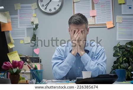 Exhausted office worker with head in hands sitting at his office desk.