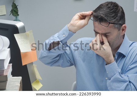 Office worker with eye pain touching his eyes and holding glasses.