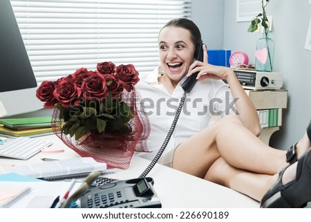 Female office worker feet up on desk talking on the phone and holding roses.
