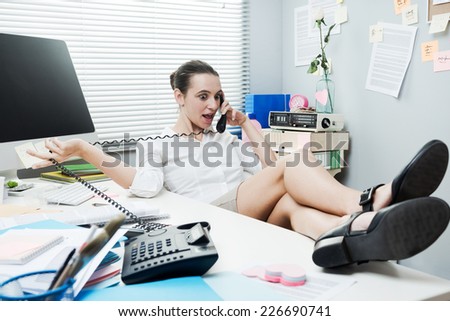 Smiling lazy woman feet up on desk talking on the phone.