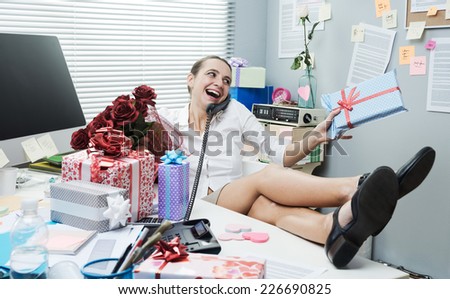 Female office worker feet up on desk talking on the phone with romantic gifts.