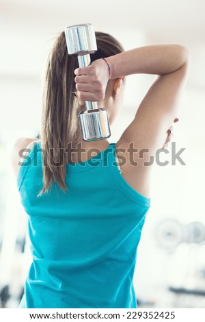 Attractive woman working out with dumbbells rear view.