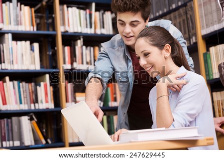 Schoolmates studying together at the library with bookshelves on background
