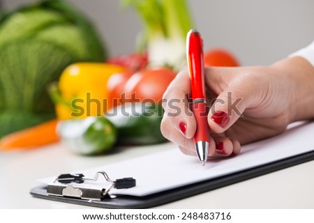 Nutritionist writing medical records and prescriptions with fresh vegetables