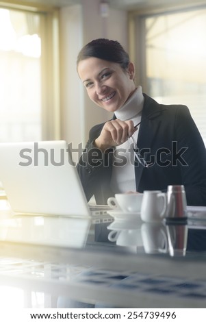Smiling young businesswoman at the bar working on her laptop