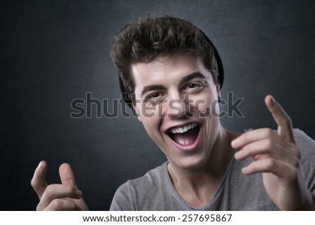 Excited cheerful young man smiling at camera with hands raised