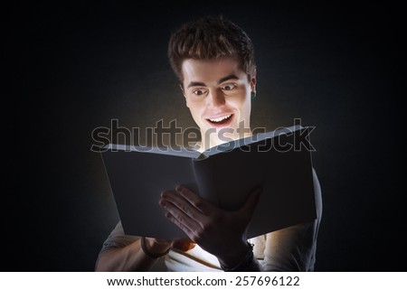 Young smiling man reading an exciting book glowing in the dark