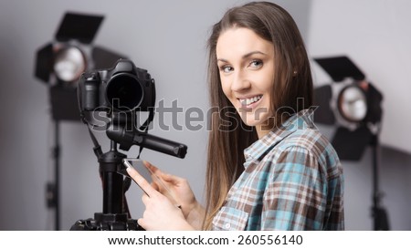 Young female photographer posing with a digital camera on tripod and lighting equipment on background