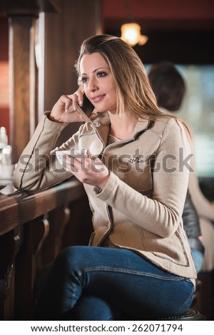 Beautiful girl sitting at the bar counter and having a phone call with her mobile phone