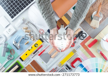 Man\'s hands close up holding a CFL energy saving lamp, work and repair tools on background, top view