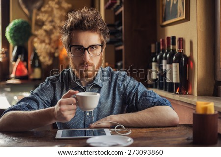 Nerd hipster guy with glasses sitting at bar table and using a tablet