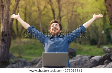 Happy cheerful hipster man with a laptop sitting outdoors in nature, freedom and happiness concept