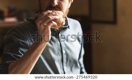 Hungry young hipster man eating a tasty sandwich with ham, hand close up