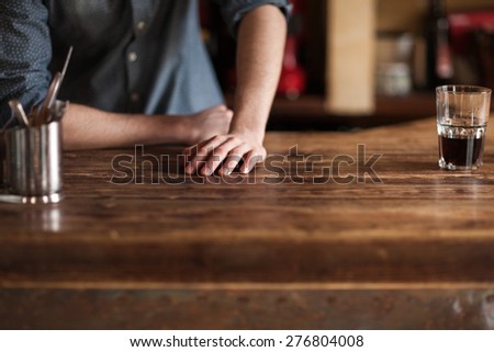 Young barman leaning on wooden bar counter hands close up, unrecognizable person