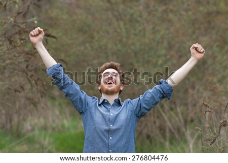 Cheerful happy hipster guy with raised fists, plants and vegetation on background, freedom and nature concept