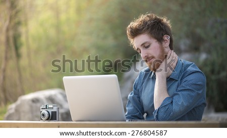 Young hipster man working with his laptop outdoors in nature, trees and plants on background