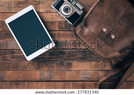 Vintage contemporary traveler and tourist equipment on a table, leather bag, camera and digital tablet, top view