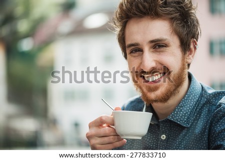 Funny cheerful guy having a cappuccino at the bar with milk moustache, smiling at camera