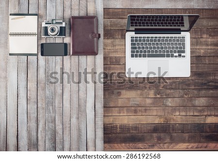 Grunge hipster wooden desktop with vintage camera, computer, organizer, mobile phone and notebook, blank copy space