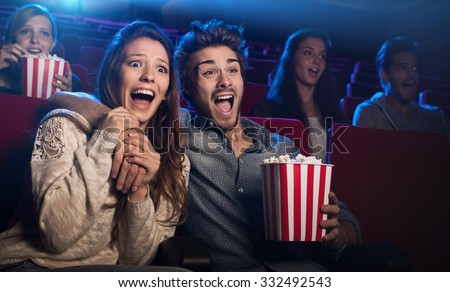 Young scared couple at the cinema watching an horror movie and screaming, she is holding her boyfriend's hand Imagine de stoc © 