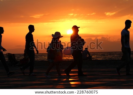 City crowd. Rush. People walking by the sea at sunset. Silhouette of people walking by the sea at sunset