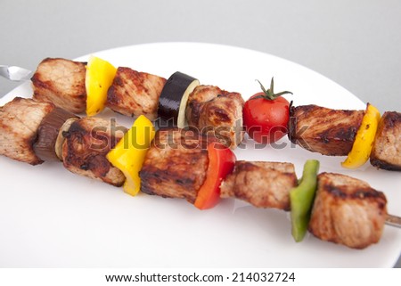 On a white plate kebab, fried pepper and tomatoes.