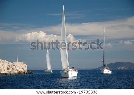 four yachts sail on the sea near the rock