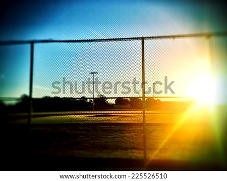 A football field at sunset surrounded by a chain-link fence.