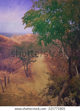 A dirt country lane winds between trees through the hills.