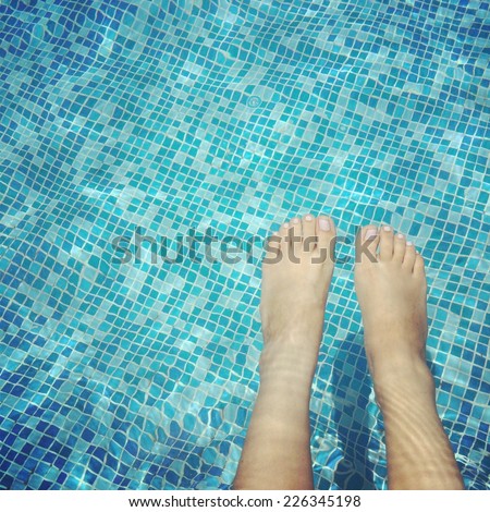 A pair of legs and feet dangling in a swimming pool.