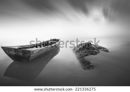 black and white Image of the boat and the stone when haze occur at the sea . Motion blur effect at sky . Image has grain or noise and soft focus when view at full resolution
