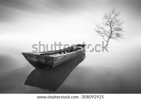 black and white Image of the boat and single tree when haze occur at the sea . Motion blur effect at sky . Image has grain or noise and soft focus when view at full resolution