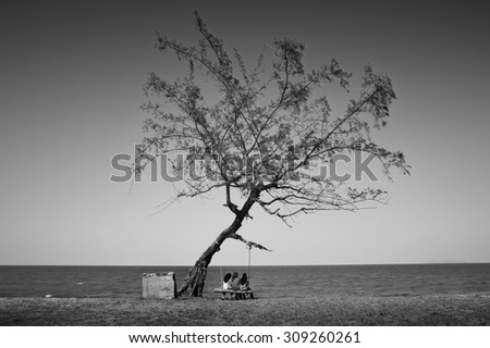 Black and white image of A person sit on the cradle next to a tree . Image has contain certain grain and soft focus