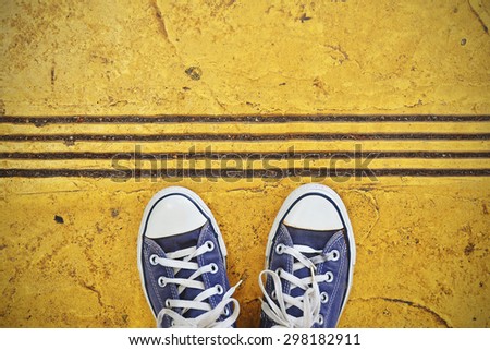 Blue Sneaker shoes standing on yellow street. Canvas shoes on street. Top view. Vintage effect.