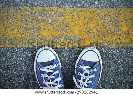 Blue Sneaker shoes standing behind the yellow line. Canvas shoes on street. Top view.