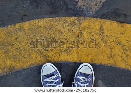Blue Sneaker shoes standing behind yellow line. Canvas shoes on street. Top view.