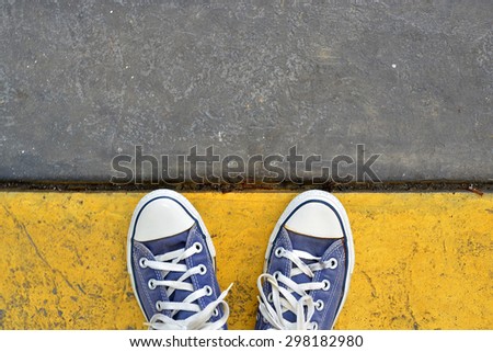 Blue Sneaker shoes standing on yellow line. Canvas shoes on street. Top view.