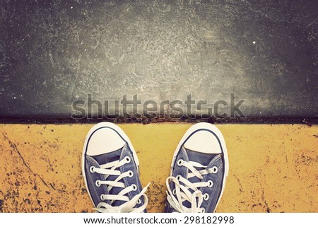 Blue Sneaker shoes standing on yellow line. Canvas shoes on street. Top view. Vintage effect.