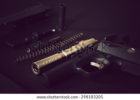 Disassembled handgun on black background. Separate 11 mm or 0.45 Pistol Parts. Shallow depth of field. Vintage effect.