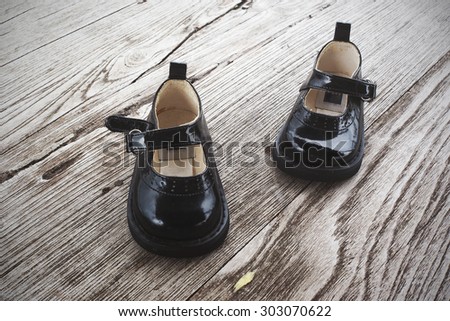 Black patent leather baby shoes on wooden background. Toned image.
