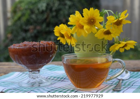 Tea in a glass cup, jam and a bunch of yellow flowers