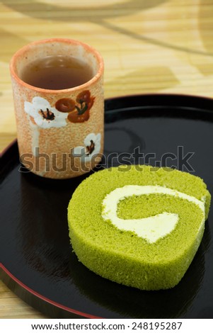 Green tea jam roll cake with hot tea ceramic cup.