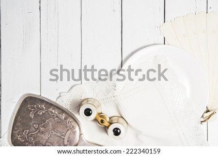 Vintage classic composition with antique binoculars, ivory fan and ceramic plate and cotton white napkin a white wooden background shabby chic style dance theme