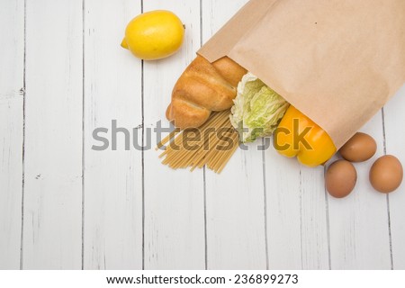 Food from supermarket in a paper craft bag on a white wooden background.