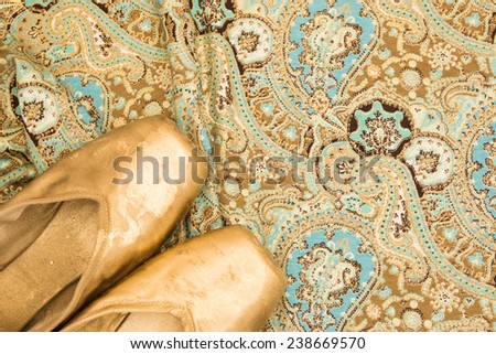Colored golden old ballet shoes pointe on a oriental Indian cloth background with golden floral pattern