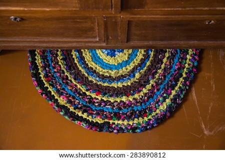 Colorful hand made knitted rug under a antique cabinet. Reuse of colorful flap. Folk nation creativity. Rustic style. Rough texture and bright design