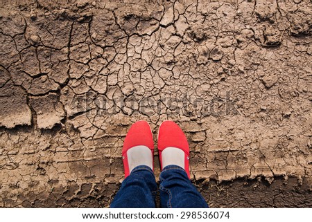 Woman foot in red shoes and jeans standing on a cracking clay ground