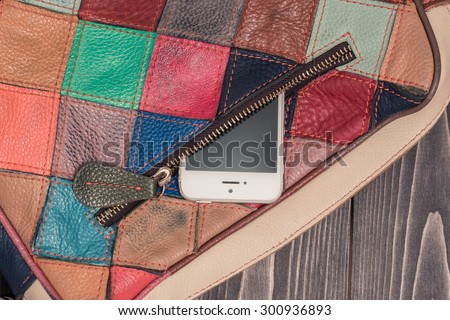 Stylish bright leather bag of square colorful patches. Close-up photo with pocket and zipper and a phone inside