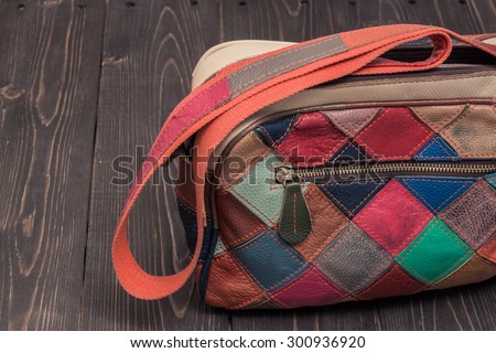 Stylish bright leather bag of square colorful patches on a dark wooden background