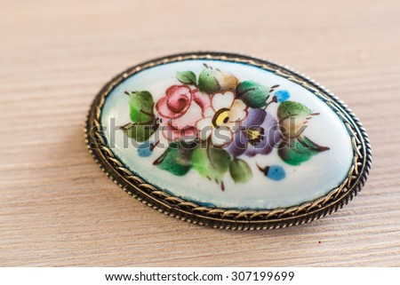 Silver enamel brooch in russian national style painted with flowers on a wooden background